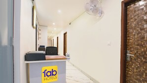 Un espace d’accueil d’hôtel avec un comptoir de réception portant l’inscription « fab HOTELS », un ventilateur blanc au plafond et une porte en bois sur la droite.