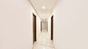 Un couloir aux murs blancs et au sol en marbre, qui mène à un espace de bureaux.