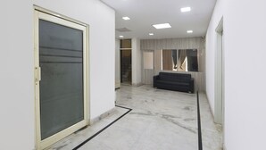 A hallway with a sliding glass door, a black sofa, and a staircase leading to another level. - Fabhotel The New Moon (New Delhi)