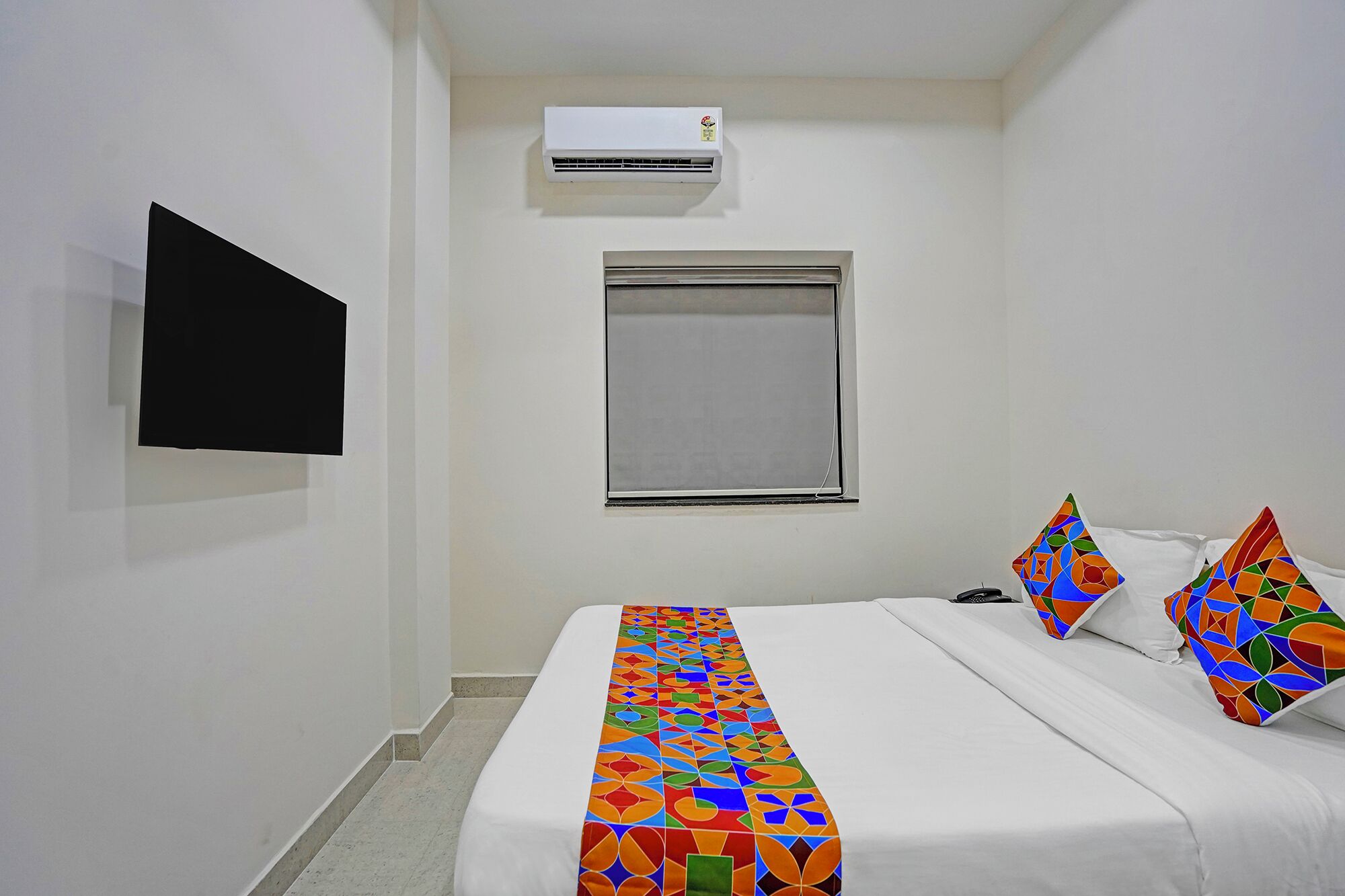 Habitación de hotel con cama, ventana, aire acondicionado y televisor montado en la pared.
