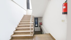 Un escalier avec une rampe métallique mène à une porte. Un extincteur rouge est fixé au mur, à droite.