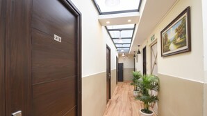 A hallway with wooden flooring, a skylight, potted plants, and a painting on the wall. - Via The Heights (New Delhi)
