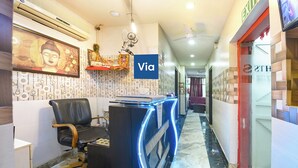 A reception area with a desk, a chair, a Buddha statue, and a wall with patterned wallpaper. - Via The Heights (New Delhi)