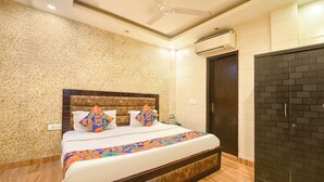 A bedroom with a patterned wall, a bed with colorful geometric pillows, a ceiling fan, an air conditioning unit, and a brick-patterned wardrobe. - Via The Heights (New Delhi)