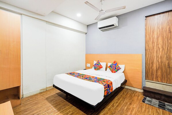 A hotel room with a bed, a ceiling fan, an air conditioning unit, and a wooden wardrobe. - Fabhotel The Park View (Surat)