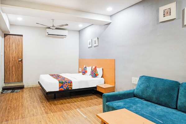 Une chambre d’hôtel avec un lit, un canapé bleu, une armoire en bois, un ventilateur de plafond et un appareil de climatisation.