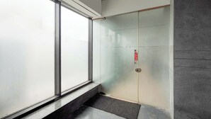 Un ascensor moderno con puerta de vidrio, un botón rojo de emergencia y una pequeña zona alfombrada en la parte inferior.