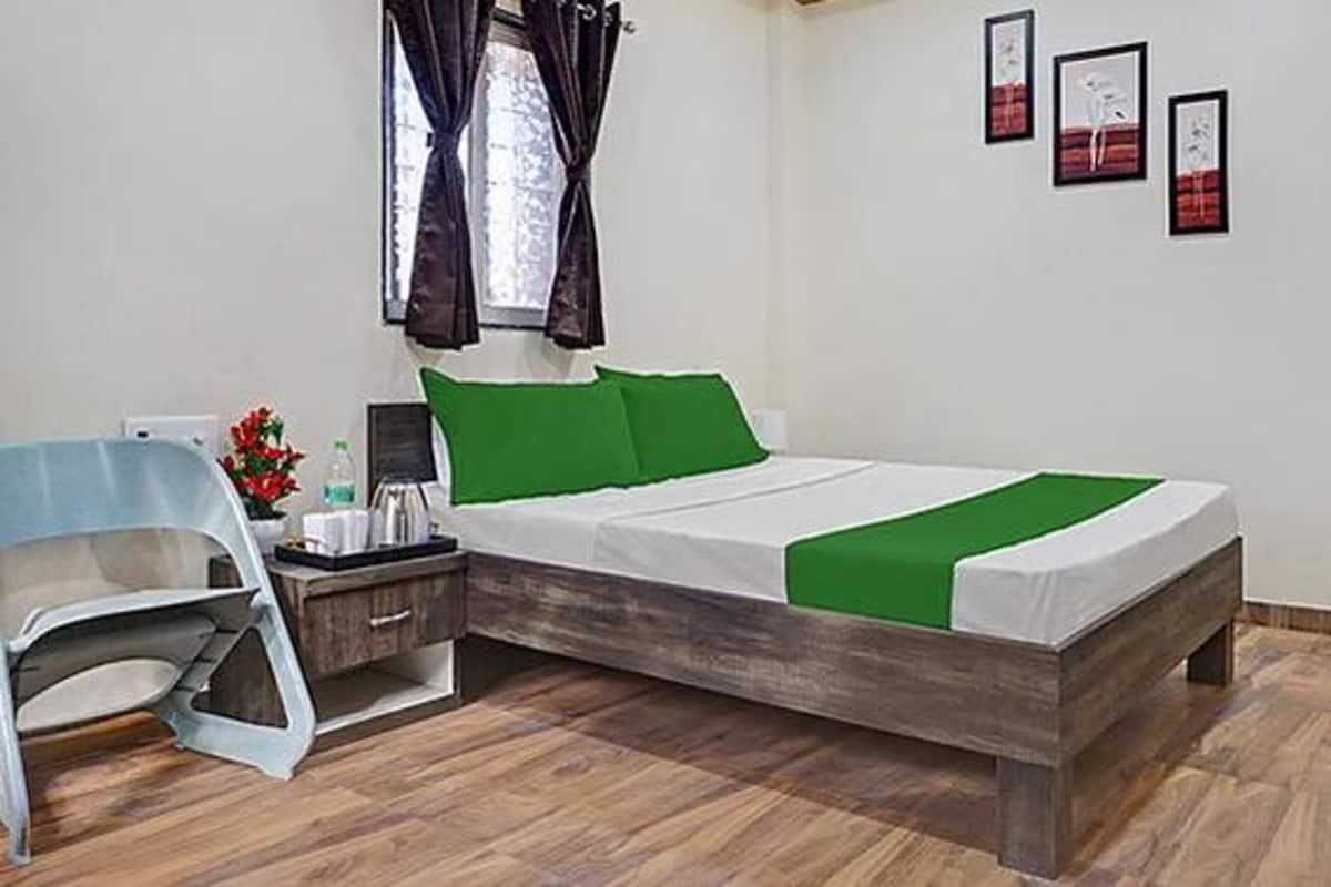 A neatly arranged bedroom with a wooden bed, green pillows, a bedside table with a lamp, and a chair.