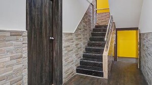 A staircase with a wooden door on the left, a yellow wall on the right, and a stone wall on the left. - Fabhotel Stay One (Mawal)