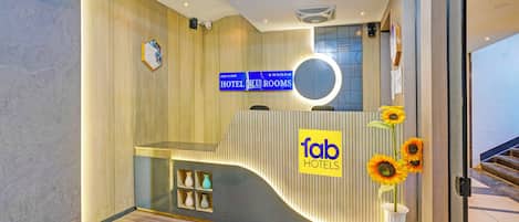 A hotel reception area with a modern design, including a reception desk, a sign for 'fab hotels', and a staircase leading to the second floor.
