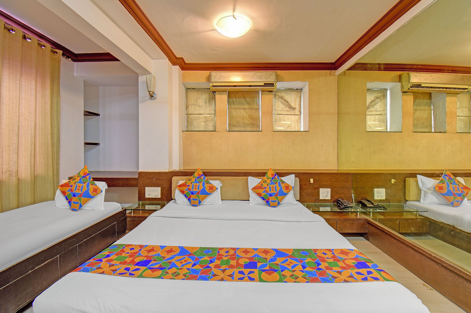 A hotel room with a large bed, multiple pillows, a bedside table, a mirror, and air conditioning units.