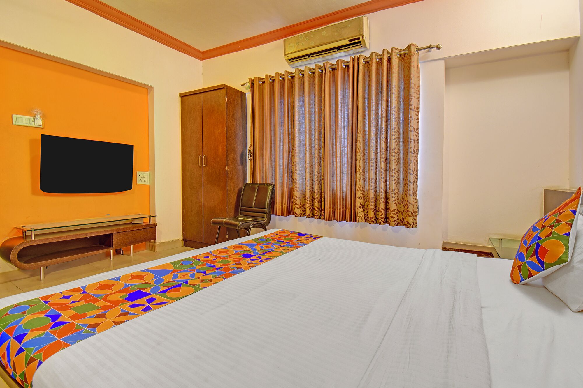 A hotel room with a large bed, a TV mounted on the wall, a wardrobe, and a chair.