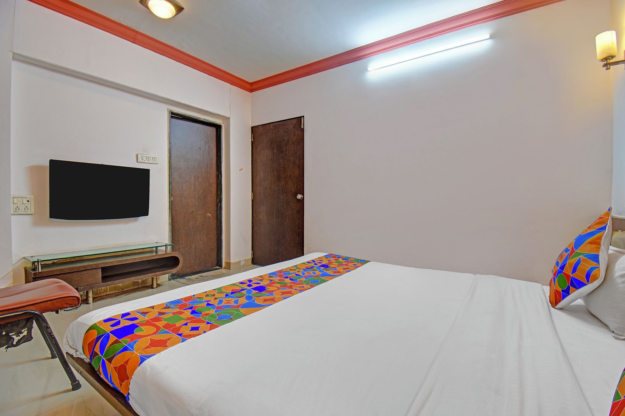 A hotel room with a bed, a television mounted on the wall, a wooden door, and a bench.