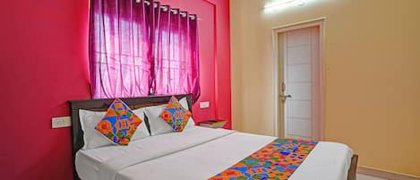 A bedroom with a bed, a window with curtains, a door, and a bedside table.