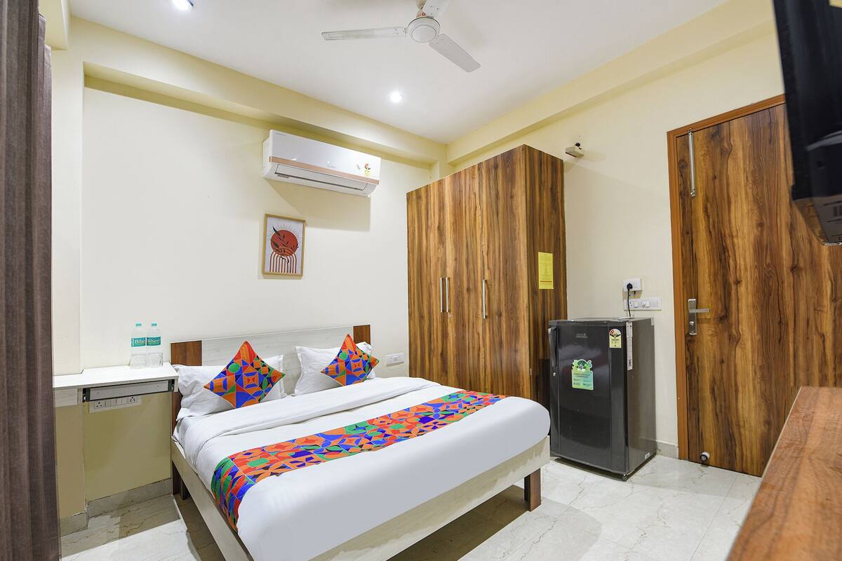 A hotel room with a bed, a wardrobe, a refrigerator, and an air conditioning unit.