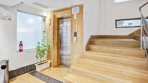 Rebedor d'hotel amb una escala de fusta, un ascensor, un extintor i una planta en test.