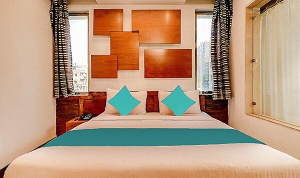 A hotel room with a large bed, two pillows, a wooden headboard, and curtains.
