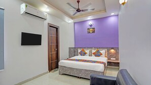 A bedroom with a bed, a ceiling fan, a TV, and a purple accent wall. - Fabhotel Moonlit (Noida)