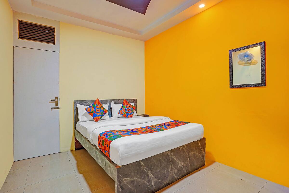 A hotel room with a bed, a door, a vent, and a framed picture on the wall.