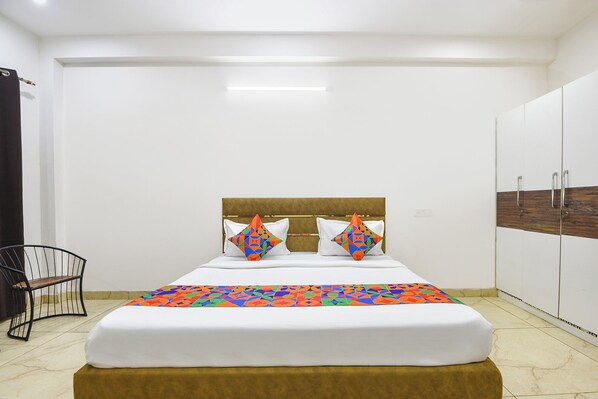 Een net opgemaakt bed met een bedsprei met een patroon, twee kussens met geometrische motieven, een houten hoofdbord en een garderobe met een houten accentpaneel.