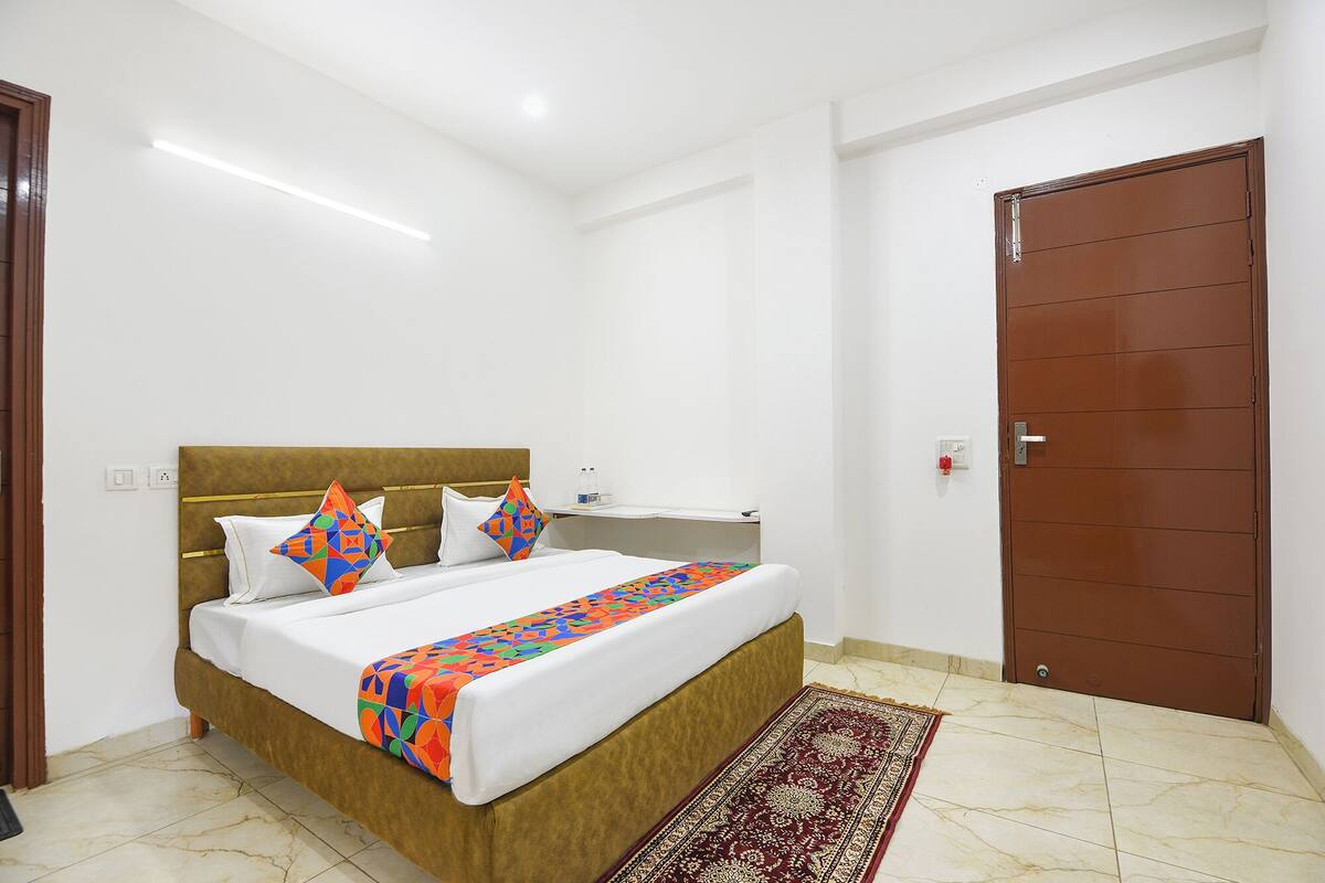 A hotel room with a bed, a nightstand, a brown door, and a patterned rug.
