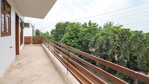 Un balcón con suelo de baldosas y baranda de madera, con vistas a una zona verde exuberante con árboles.