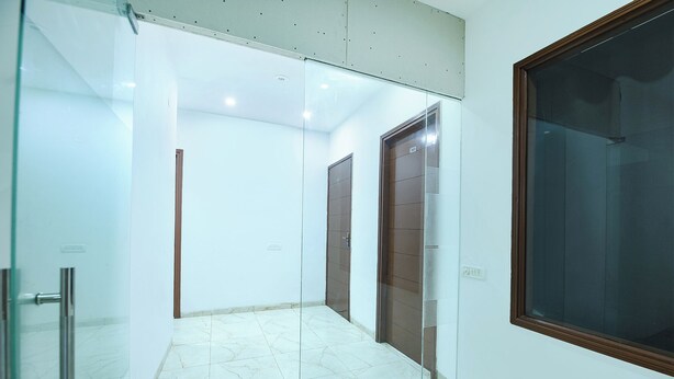 Un pasillo con una puerta de cristal a la izquierda, un ventanal grande a la derecha y suelo de baldosas.