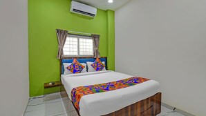 A bedroom with a bed, green walls, a window with curtains, and an air conditioning unit. - Fabhotel Stay Inn Lodge (Pune)