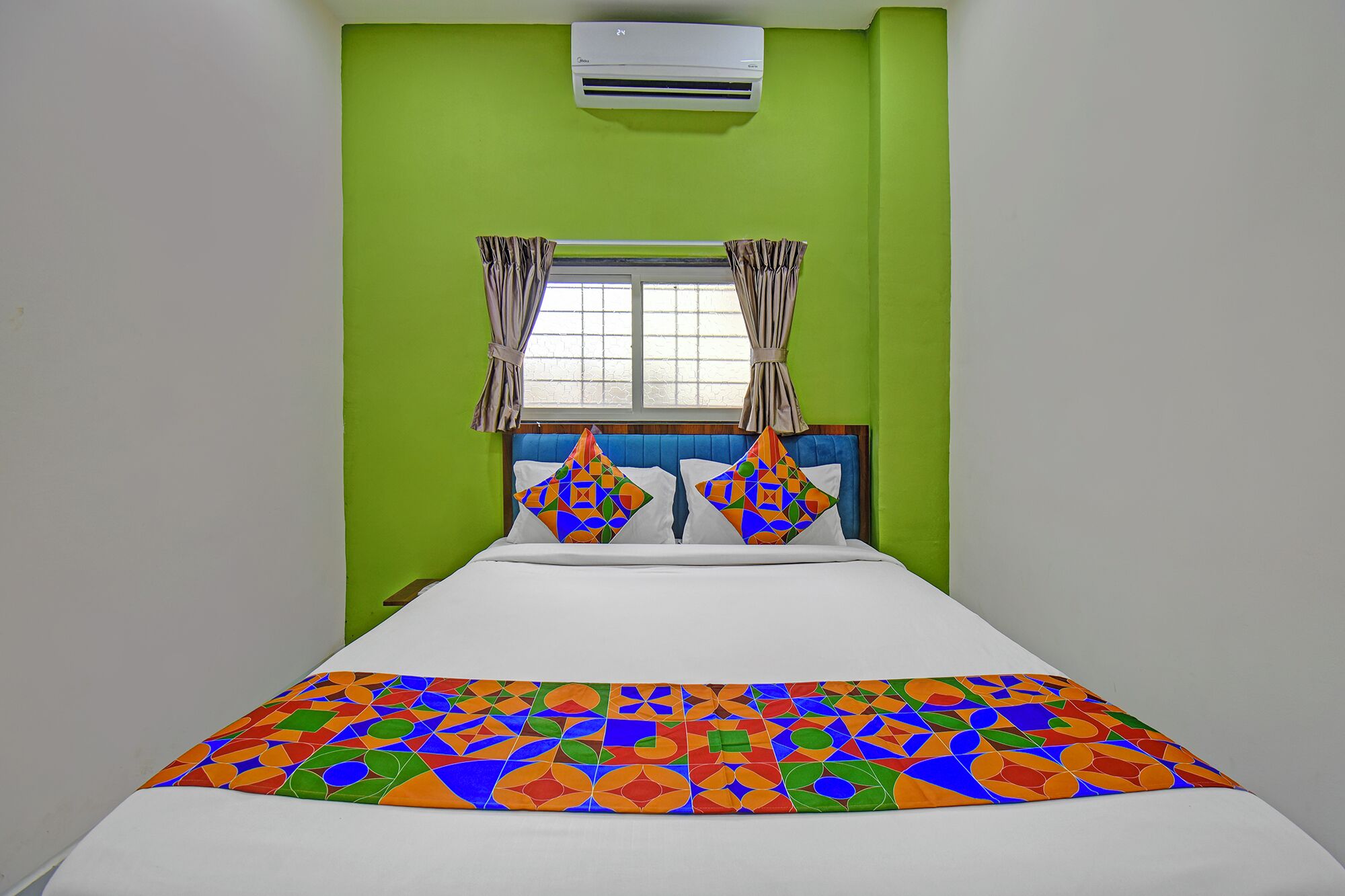 A room with a bed, green walls, a window with curtains, and an air conditioning unit.