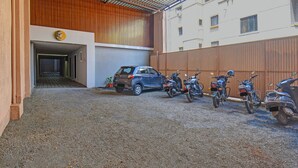 A parking area with a gravel surface, a blue SUV, and several motorcycles parked against a wooden fence. - Fabhotel Stay Inn Lodge (Pune)
