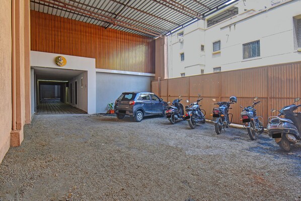 A parking area with a gravel surface, a blue SUV, and several motorcycles parked against a wooden fence. - Fabhotel Stay Inn Lodge (Pune)