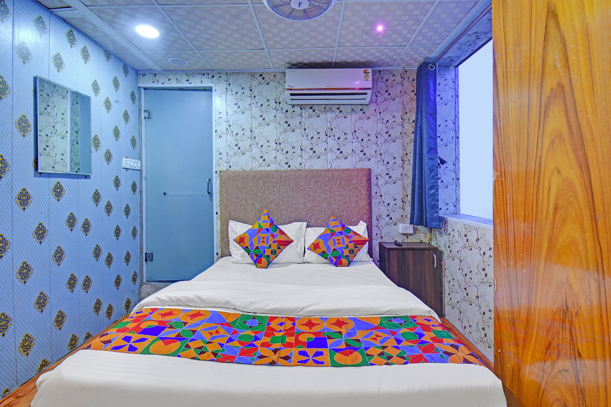 A room with a bed, a nightstand, a window, and an air conditioning unit.