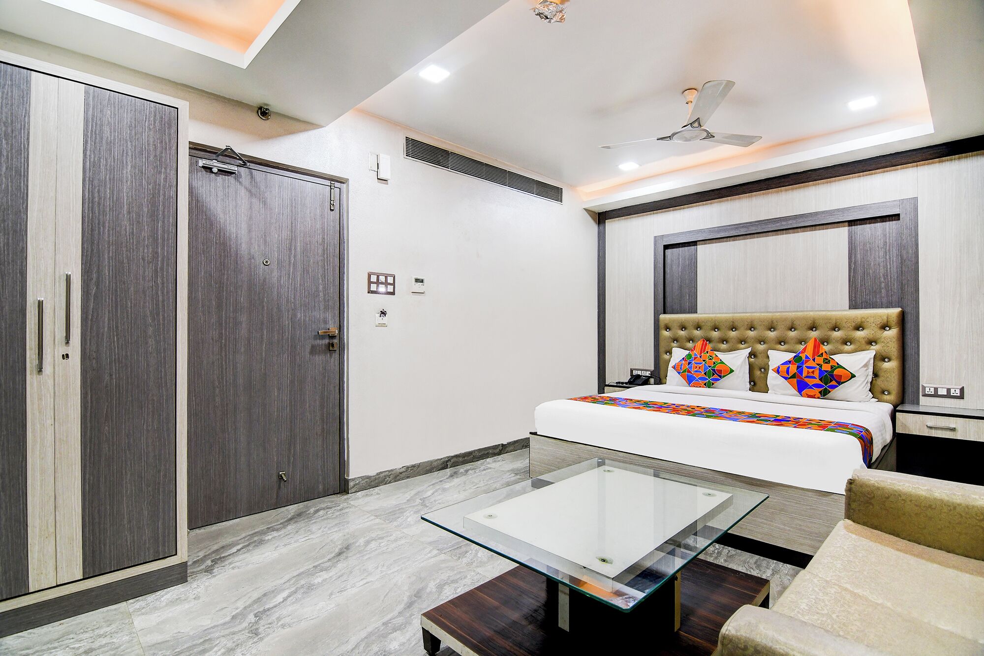 A modern hotel room with a bed, a glass coffee table, a sofa, and a wardrobe.