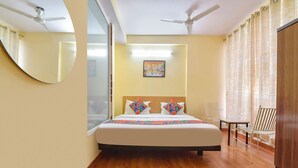 A hotel room with a bed, two chairs, a painting on the wall, and a ceiling fan. - Fabhotel Silver Stay 02 (Jaipur)