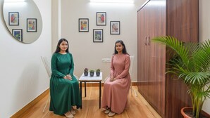 Two women seated in a room with a wooden floor, a white table with potted plants, and a large wooden cabinet. - Fabhotel Silver Stay 02 (Jaipur)