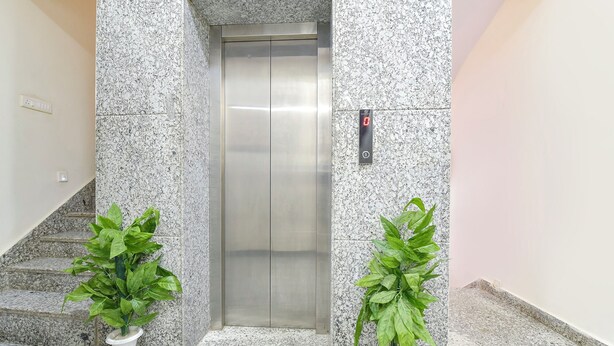 An elevator in a hallway with granite walls, two potted plants, and a staircase to the left. - Fabhotel Silver Stay 02 (Jaipur)