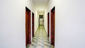 A hallway with white walls, red and black patterned doors, and a marble floor. - Fabexpress Elvin Balaji Beach Palace (Calangute)