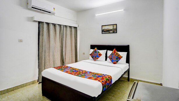 A hotel room with a bed, a small table, an air conditioner, a window with curtains, and a picture on the wall. - Fabexpress Elvin Balaji Beach Palace (Calangute)