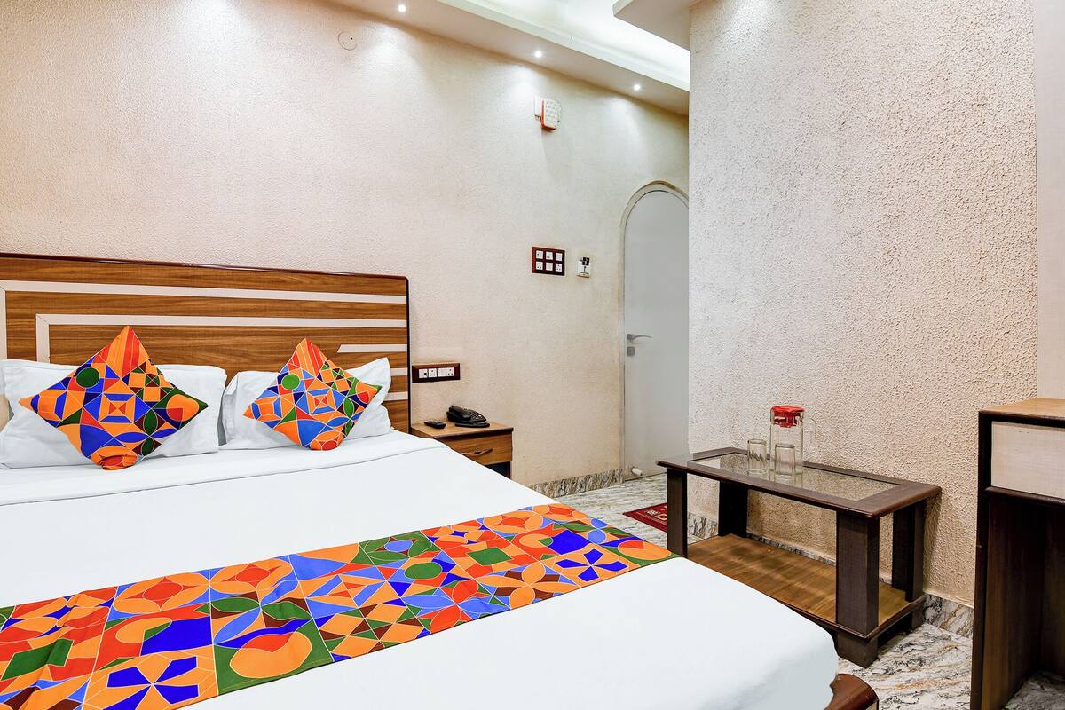 A hotel room with a large bed, a wooden headboard, a nightstand, a bedside table with a lamp, and a door with a handle.