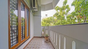 A narrow corridor with tiled flooring, a potted plant, and a window with a metal grill. - Fabhotel Martine Residency - French Colony, 5 Mins from Rock Beach (Puducherry)