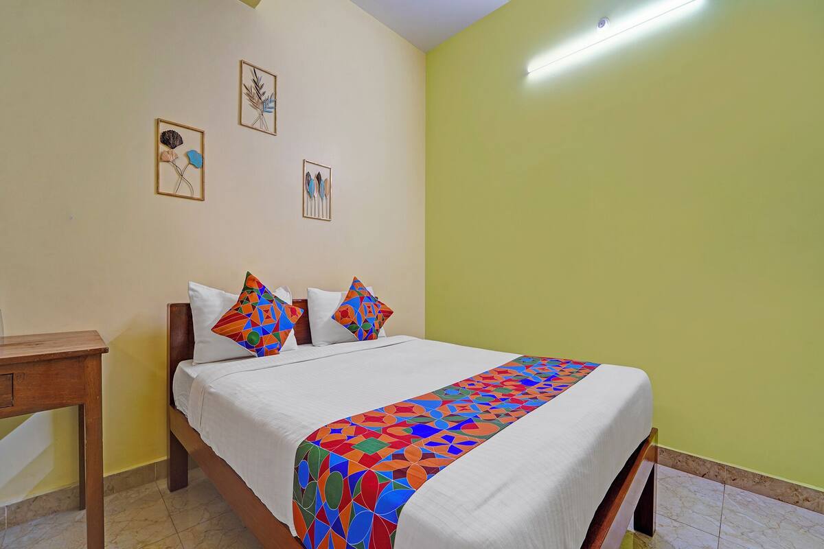 Una cama bien hecha con un edredón y almohadas de estampado geométrico y colores vivos, una mesita de noche de madera y una pared con tres cuadros enmarcados.