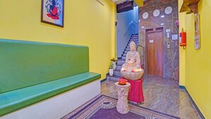 Un espace d’accueil avec un banc vert, une statue de Bouddha, une horloge et un extincteur.
