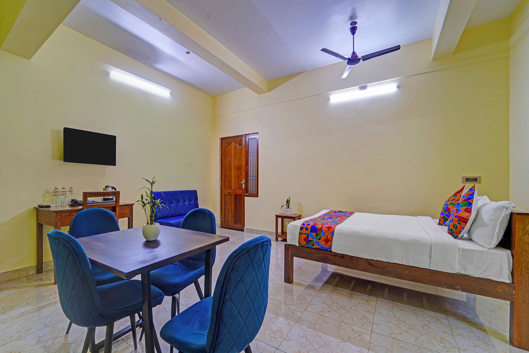 A hotel room with a bed, a desk with chairs, a television, and a ceiling fan.