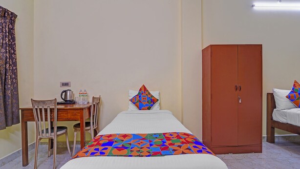 Une chambre d’hôtel avec un lit, un bureau en bois avec une bouilloire, deux bouteilles d’eau, un oreiller coloré et une armoire.