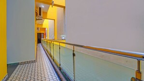 A hallway with patterned flooring, a glass railing, and a yellow wall. - Fabhotel Martine Residency - French Colony, 5 Mins from Rock Beach (Puducherry)