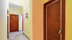 A hallway with a marble floor, a wooden door with a number plate, and a wall-mounted light fixture. - Fabhotel Vedsri (Kolkata)