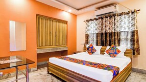 A hotel room with a wooden bed, a desk, and a window with curtains. - Fabhotel Vedsri (Kolkata)