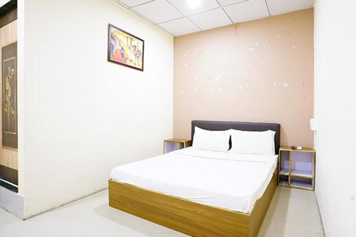 A neatly made bed in a hotel room with a plain wall and a single framed picture.