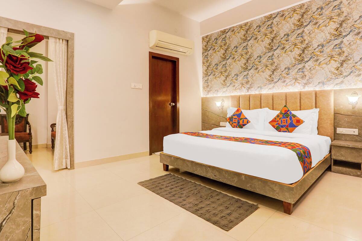 A hotel room with a bed, a nightstand, a wall-mounted lamp, and a floral-patterned wall.