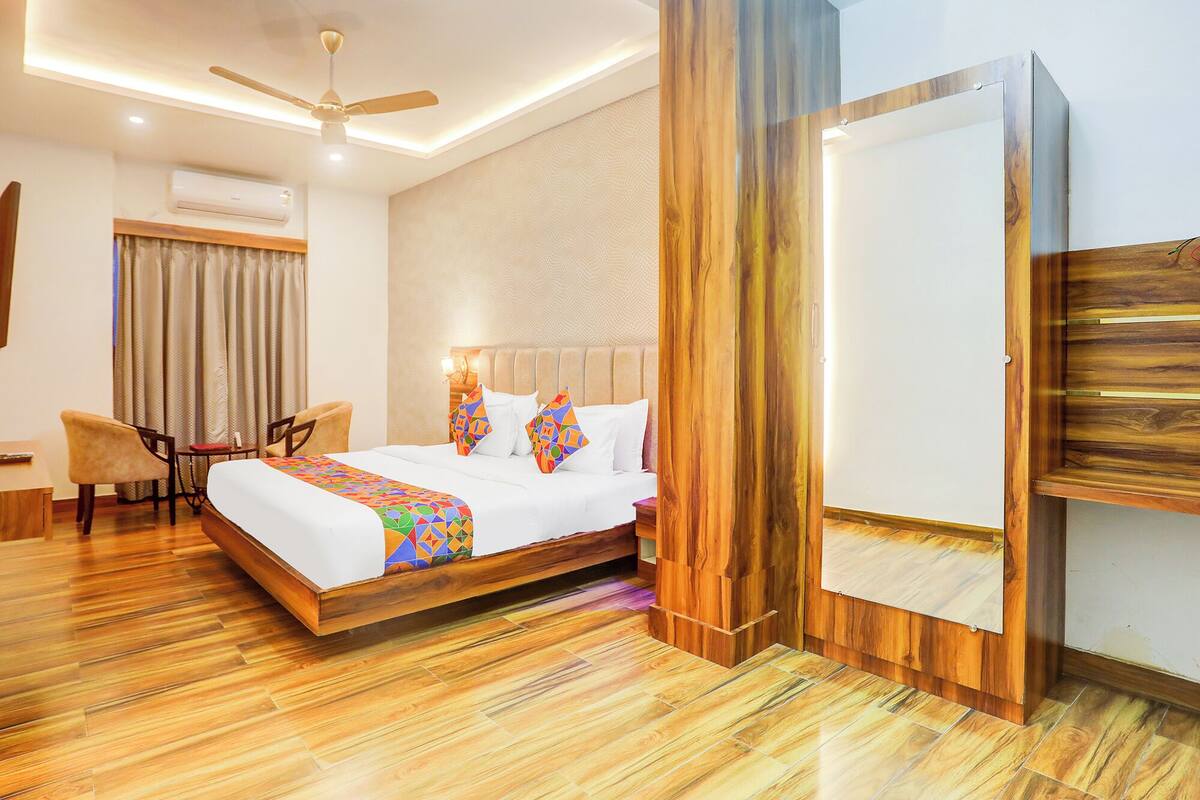 A hotel room with a bed, a chair, a desk, an air conditioning unit, and a ceiling fan.